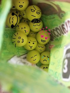 some yellow balls with faces drawn on them in a green bag next to a package of chocolate