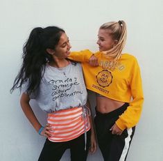 two young women standing next to each other near a white wall and one has her arm around the other's shoulder