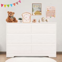 a teddy bear sitting on top of a white dresser in a child's room