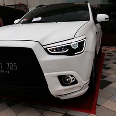 the front end of a white car parked on a checkered tile flooring area