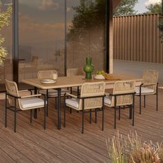 an outdoor dining table and chairs on a wooden deck with glass walls in the background