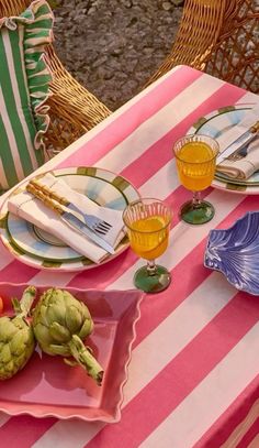 an outdoor table set with plates, glasses and fruit on top of striped pink and white cloth