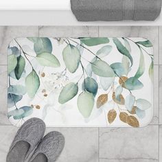 a bathroom rug with leaves on it next to a pair of slippers and a towel