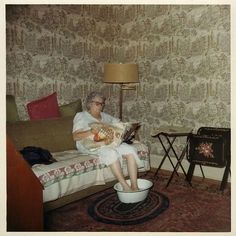 an old woman sitting on a couch with a cat in her lap, reading a book