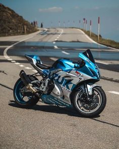 a blue and silver motorcycle parked on the side of an empty road next to water