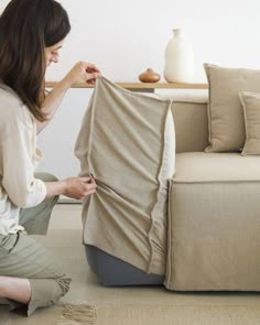 a woman sitting on the floor next to a couch holding up a piece of cloth