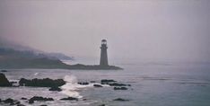 a light house sitting on top of a rock covered beach next to the ocean with waves crashing in front of it