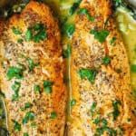 two cooked salmon fillets in a pan with herbs