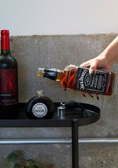 a person pouring liquor into a bottle on top of a black table next to a plant