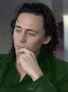 a man with long black hair and blue eyes is looking at the camera while wearing a green shirt