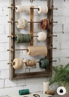 an old wooden frame with yarn and scissors hanging on it's side in front of a white brick wall