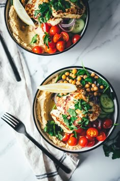 two bowls filled with hummus, tomatoes, chickpeas and cucumbers