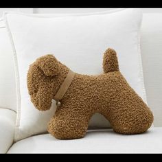 a brown dog pillow sitting on top of a white couch next to a stuffed animal