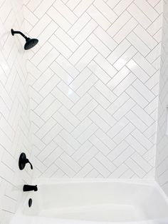 a bathtub with black fixtures and white tile in the shower area, along with two faucets