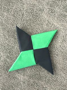 a green and black origami star laying on top of a gray carpeted floor