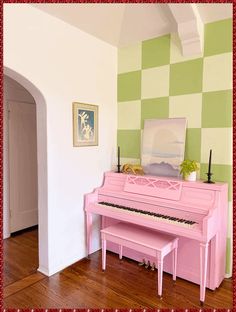 a pink piano sitting in front of a green and white checkerboard wall next to a doorway