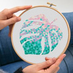 a person holding up a cross - stitch pattern on a wooden hoop with the image of a palm tree