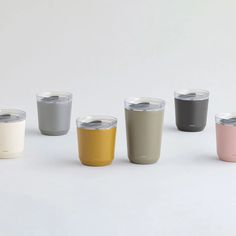 four different colored tumblers sitting next to each other on a white surface with one cup in the middle