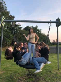 a group of young people sitting on top of a swing set in a park together