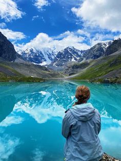 a woman sitting on the edge of a lake looking at mountains