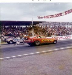 an old photo of a drag car going around a track with people watching from the stands