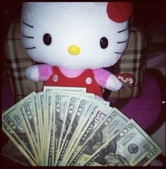 a hello kitty stuffed animal sitting on top of a pile of money next to $ 100 bills