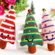 three crocheted christmas trees sitting next to each other on a white surface with flowers in the background