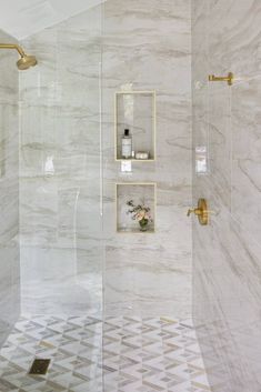 a bathroom with white marble walls and gold fixtures on the shower head, toiletries and shelves