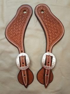 two brown and white leather shoes with silver buckles on the sides, sitting on top of a bed