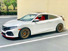 a white car with gold rims parked in a parking lot next to a building