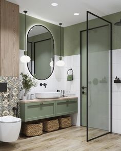 a bathroom with green and white walls, wooden floors and a round mirror above the sink