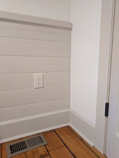 an empty room with wood flooring and white painted walls, along with a vent in the wall