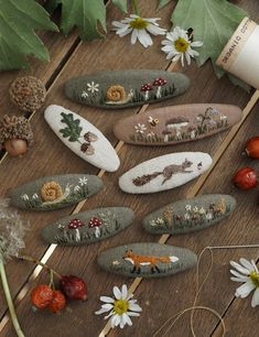 several embroidered rocks sitting on top of a wooden table next to some flowers and leaves