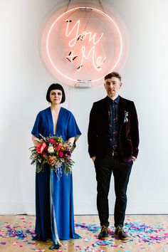 a man and woman standing in front of a neon sign with confetti on it