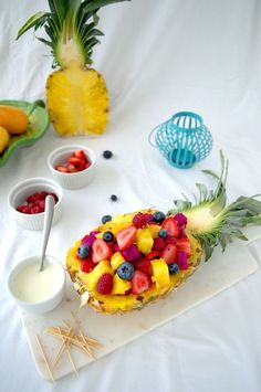 a pineapple topped with fruit next to bowls of yogurt