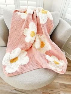 a crocheted blanket with white flowers on it sitting on a gray chair next to a window