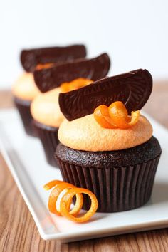 three cupcakes on a white plate with orange peels and chocolate icing