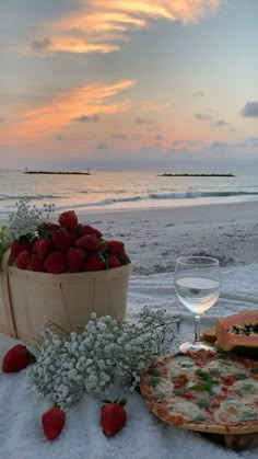 a bowl of strawberries next to two pizzas and a glass of wine on the beach