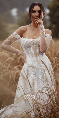 a woman in a white dress is standing in tall grass and talking on her cell phone