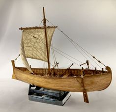 a wooden model boat with sails and ropes on a white background, sitting on top of a stack of books