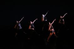 dancers in the dark with their arms up and one leg bent out, while another person is