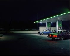 two cars are parked in front of a gas station at night with the lights on