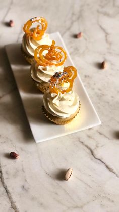 three cupcakes with white frosting and orange slices on a small square plate