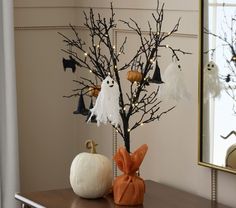 a decorated halloween tree with white pumpkins and ghost decorations on it, in front of a mirror