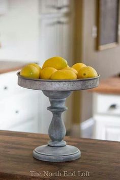 a metal bowl filled with lemons on top of a wooden table in a kitchen