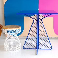 a blue table with a wooden stool next to it and a colorful wall in the background