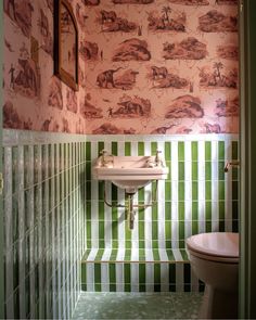 a green and white tiled bathroom with a sink, toilet and wallpapered walls