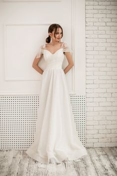 a woman standing in front of a white brick wall wearing a wedding dress with short sleeves