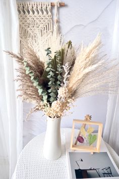 a white vase filled with lots of flowers on top of a table next to a photo frame