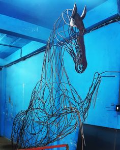 a sculpture of a horse made out of wires in a room with blue walls and flooring